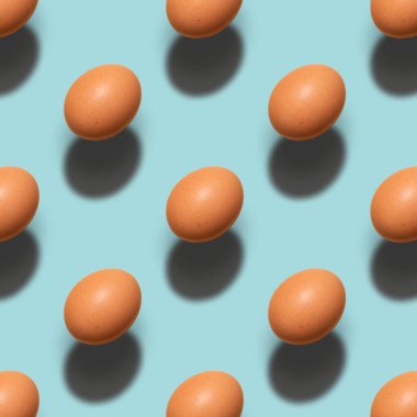 Pattern of brown chicken eggs on a blue background. Minimalism easter, food pattern with hard light and shadows.