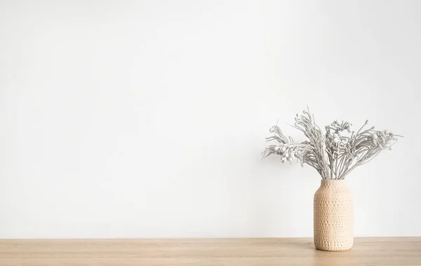 Kuru çiçekler, ahşap masanın üzerindeki vazoda beyaz bir duvarın arka planına çiçek dalları dikiyorlar. Kopya alanı ile minimal İskandinav arkaplan modeli.