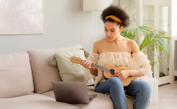 Afrikalı Amerikalı bir kadın evde dizüstü bilgisayarla ukulele müzik gitar dersleri alıyor. Bir müzik aleti çalmayı öğrenmek.
