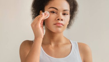 Siyah Afro-Amerikalı kadın elinde pamuk ped tutarak cildi temizleyici tonikle temizliyor. Cilt bakım giderme makyaj losyonu veya mikiler su.