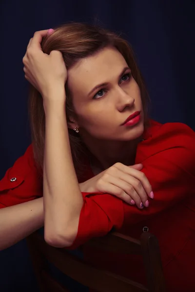 Beautiful young girl sitting on a chair in red blouse — Stock Photo, Image