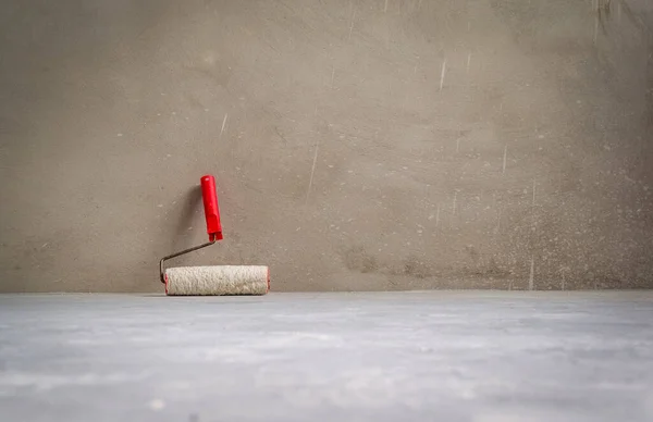Paint roller in empty room on cement floor. Grunge interior. — Foto de Stock