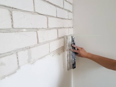 Alçıtaşı fayanslarını alçıya seriyor duvara macun bıçağıyla yapıştırıyor.