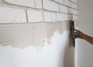 Alçıtaşı fayanslarını alçıya seriyor duvara macun bıçağıyla yapıştırıyor.