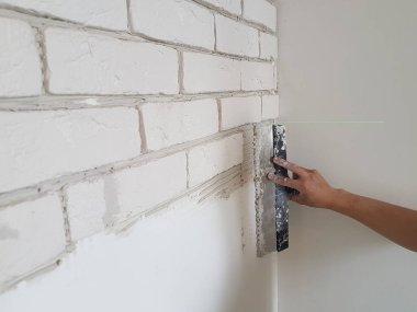 Alçıtaşı fayanslarını alçıya seriyor duvara macun bıçağıyla yapıştırıyor.