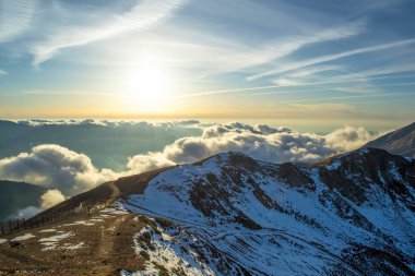 Gün batımında mavi gökyüzünde bulutların arasında karlı yüksek dağlar.
