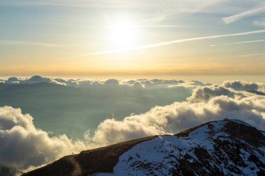 Gün batımında mavi gökyüzünde bulutların arasında karlı yüksek dağlar.