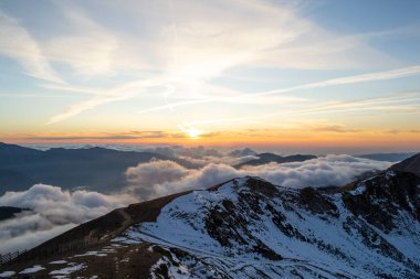 Gün batımında mavi gökyüzünde bulutların arasında karlı yüksek dağlar.
