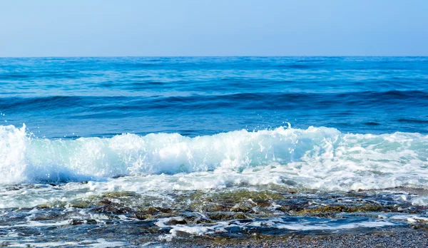 Wellen brechen an einem steinigen Strand auf und bilden Gischt — Stockfoto