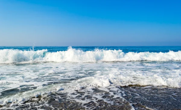 Wellen brechen an einem steinigen Strand auf und bilden Gischt — Stockfoto