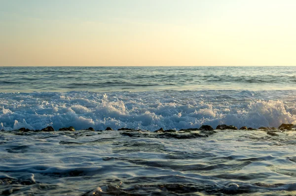 Wellen brechen an einem steinigen Strand auf und bilden Gischt — Stockfoto