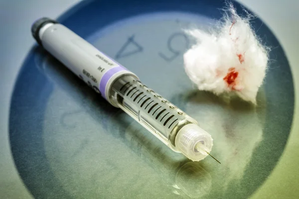 Um lápis de insulina junto com um algodão manchado com sangue — Fotografia de Stock