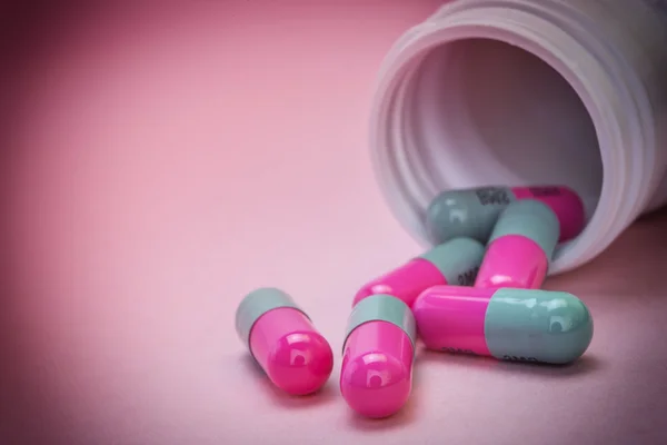 Таблетки разлива из открытой бутылки изолированы на розовом фоне — стоковое фото