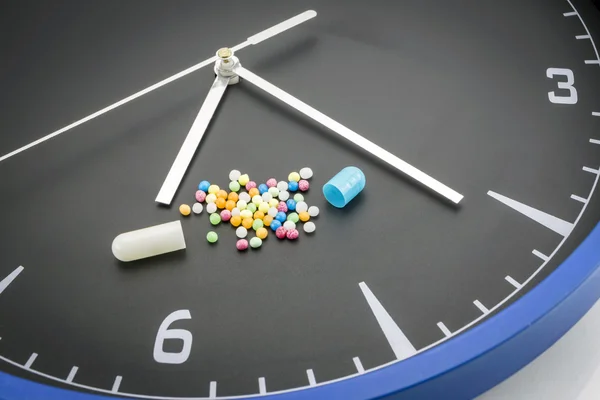 Open red capsule pill with ball color drug on black clock backgr — Stock Photo, Image