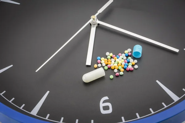 Open red capsule pill with ball color drug on black clock backgr — Stock Photo, Image