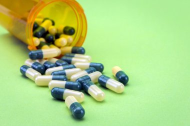 Açık bir şişe üzerinde yeşil arka plan izole dökülmesini hapları