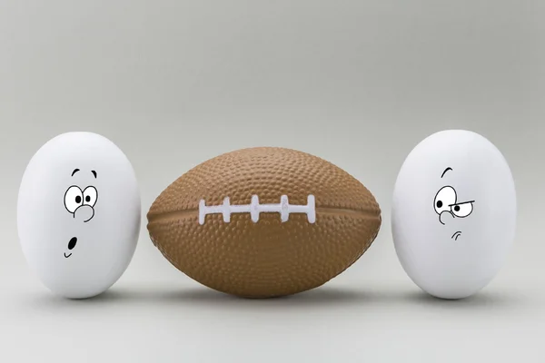 Dos huevos miran con cara extraña a un globo de rugby —  Fotos de Stock