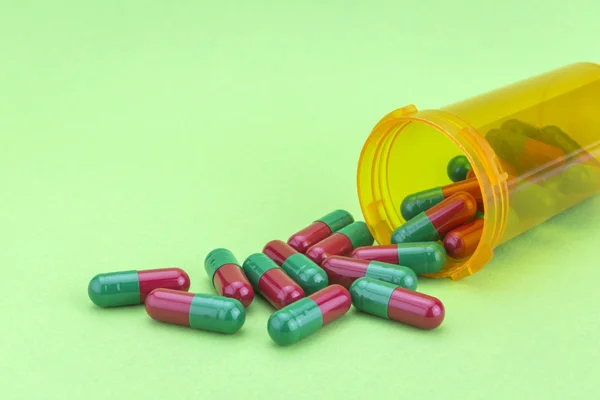 Pilules vertes et rouges se déversant d'une bouteille ouverte isolée sur gre — Photo