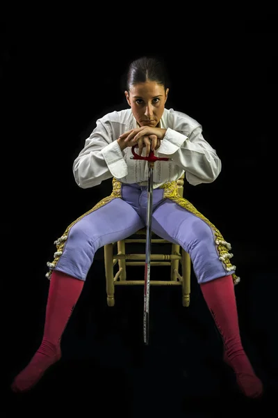 Woman bullfighter sitting on a wooden chair holding a sword — Stock Photo, Image