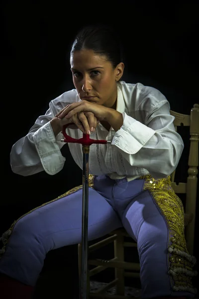 Woman bullfighter sitting on a wooden chair holding a sword — Stock Photo, Image