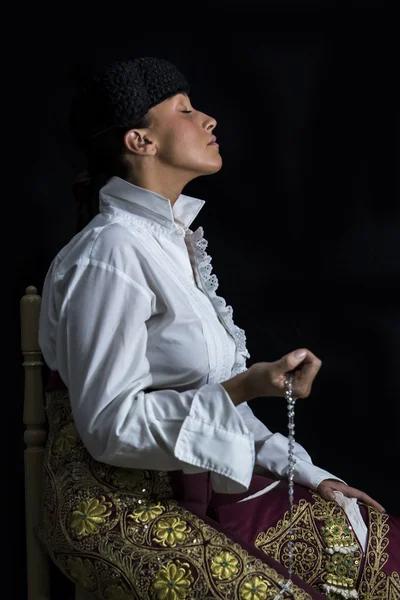 Mujer Torero en Capilla rezando con Rosario en la mano sobre fondo negro — Foto de Stock