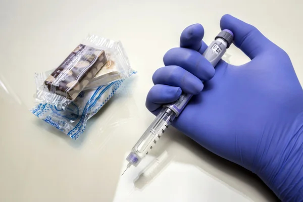 Blue-gloved hand holds a syringe of insulin together with some s