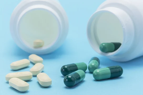 Білі таблетки з пляшки на синьому фоні — стокове фото