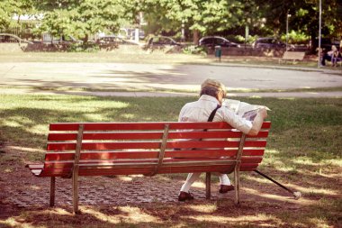 Emekli adam gazete okuyor, yaşlı adam parkta dinleniyor.