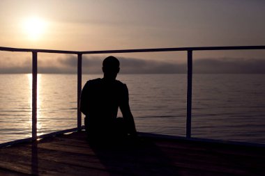 Gün batımında deniz kenarında bir adamın silueti. 