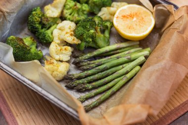 Fırında kuşkonmaz, brokoli ve parşömen kağıdında baharat ve limon olan karnabaharlar. Vejetaryen sağlıklı beslenme yemeği