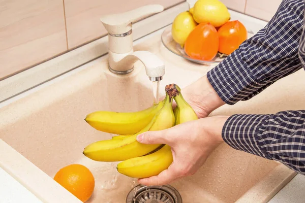 Washing fruits and food in the sink on kitchen. Hands washing bananas
