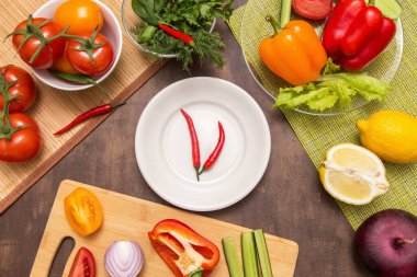 Pişirmek için farklı sebzeler ve beyaz tabakta iki kırmızı acı biber. Diyet, oruç, vegan, vejetaryen, sağlıklı baharatlı gıda konsepti