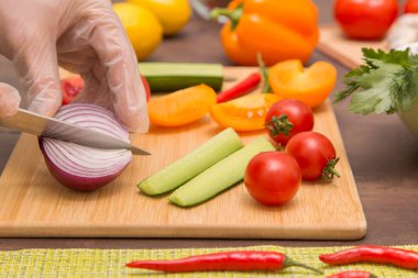 Şef sağlıklı vejetaryen diyet yemeği pişiriyor. Eldivenli eller soğan ve farklı sebzeleri kesiyor.