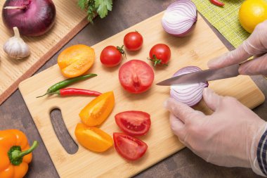 Şef sağlıklı vejetaryen diyet yemeği pişiriyor. Eldivenli eller soğan doğruyor ve salata için farklı sebzeler.