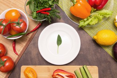 Yemek yapmak için farklı sebzeler ve boş beyaz tabakta ıspanak yeşili bir yaprak. Diyet, oruç, vegan, vejetaryen, sağlıklı gıda konsepti