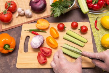 Şef salatalık kesiyor ve salataya farklı sebzeler koyuyor. Eldivenli eller sağlıklı vejetaryen diyet yemekleri pişiriyor.