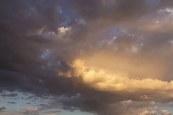 Epic sunset storm sky. Big white grey cumulus thunderstorm clouds in yellow orange sunlight on blue sky background texture