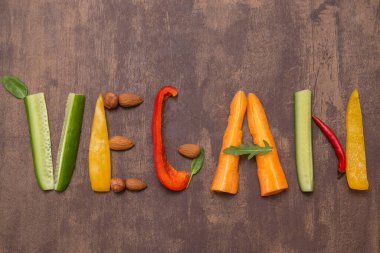 Vegan kelimesi farklı sebzelerden, meyvelerden, ahşap arka planda fındıklardan gelen mektuplarla yazıldı. Sağlıklı diyet vejetaryen yiyecekler için organik malzemeler 