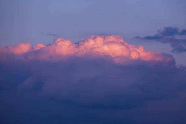 Epic sunset sunrise sky with pink big fluffy cumulus cloud in sunlight on blue sky background texture