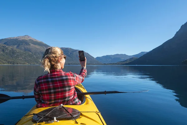 Beautiful young woman taking a selfie from her kayak to send to her friends and social networks. From Patagonia, Argentina.