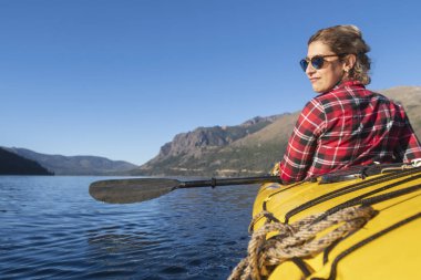Güzel bir kadın, ulusal parkın gölleri ve dağlarında tatil yaparken deniz kayığıyla kürek çekiyor..