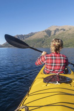 Güzel bir kadın, ulusal parkın gölleri ve dağlarında tatil yaparken deniz kayığıyla kürek çekiyor..