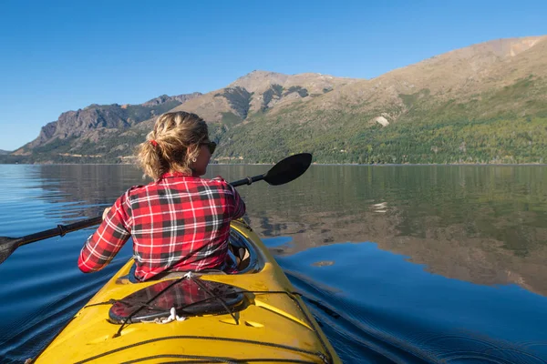 Beautiful Woman paddling a sea kayak while on vacation through the lakes and mountains of the national park.