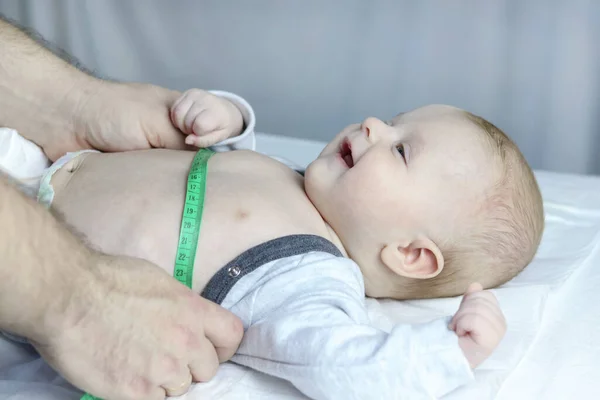 A specialist pediatrician measures the babys body with a tape measure during a screening examination, side view. Copy space - concept of child health and disease prevention, pediatrics, growth