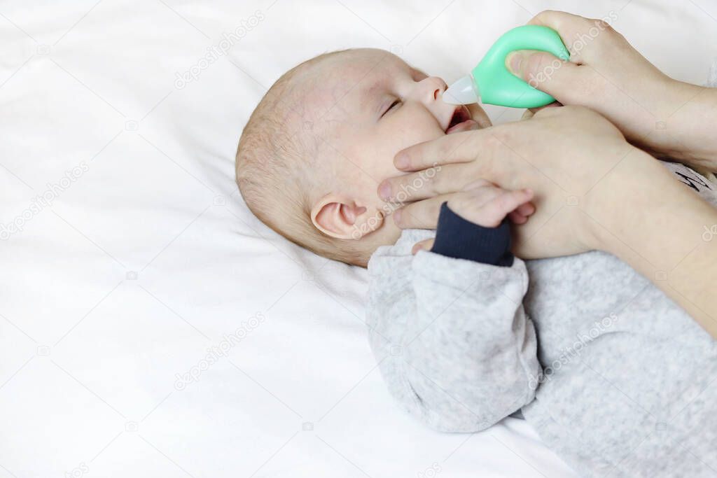 A mother uses a nasal aspirator on a sick baby, sucking mucus from the nose. Copy space - the concept of child health, colds, immunity, prevention, parental love, cleansing
