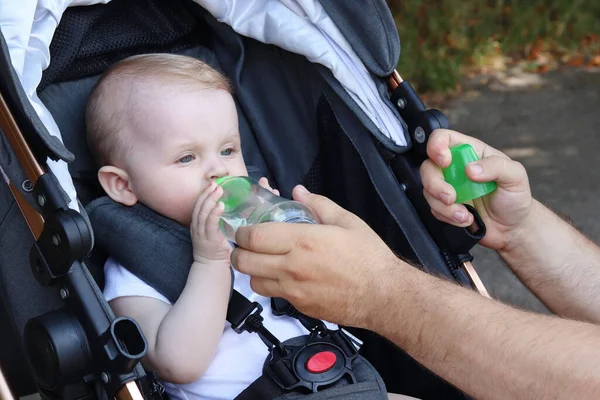 Cute baby drinks water from a baby bottle. Water balance in the body. Cold soft drinks with fruit. Copy space-concept of thirst, heat, outdoor recreation, summer refreshing drink in cans, dehydration — Stock Photo, Image