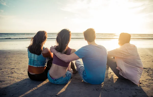 Négy barát élvezi a naplementét a strandon — Stock Fotó