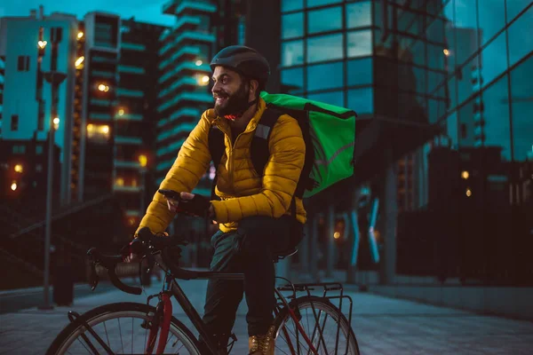 Food delivery rider on his bicycle. Image of a middle age man at work in the city center. Delivering pizza and burgers at home with the thermal backpack