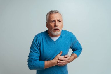 Yakışıklı son sınıf öğrencisi gri arka planda izole edilmiş. Yaşlı adam acı çekiyor. Üçüncü yaş ve kıdem kavramları