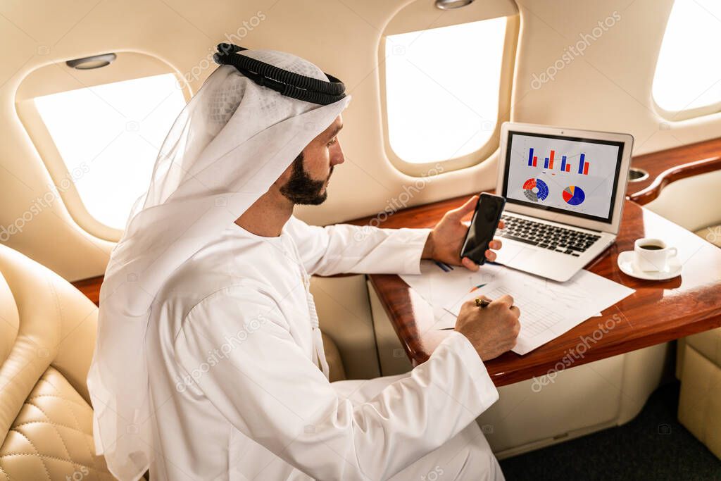 Arabic man wearing kandora in emirates style flying on exclusive private jet - Middle-eastern businessman with traditional dress flies in exclusive business class on airplane, concepts about business and trasportation